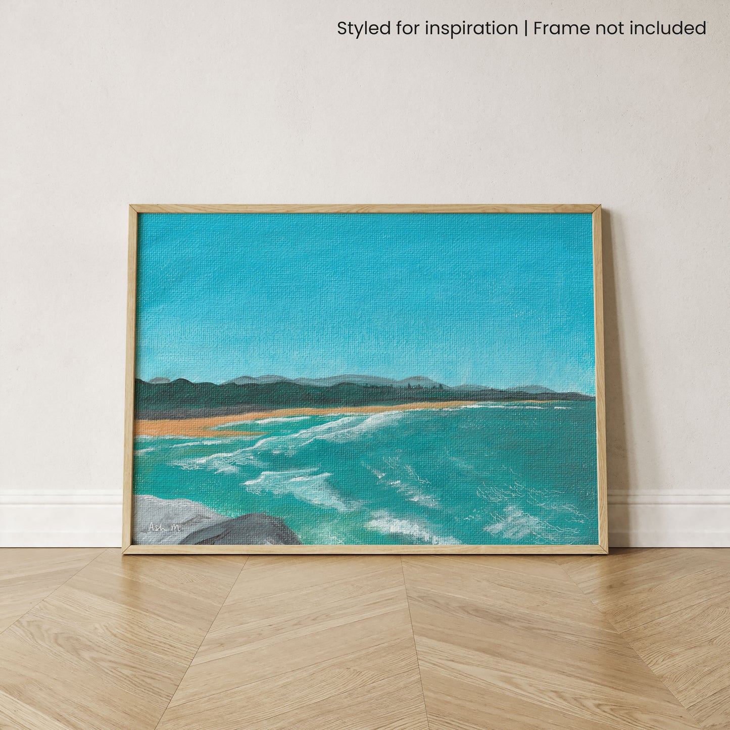 Framed painting of a coastal scene at North Wall Beach, Coffs Harbour, with blue water and waves and clear sky. It is leaning against a white wall, set upon a timber floor.