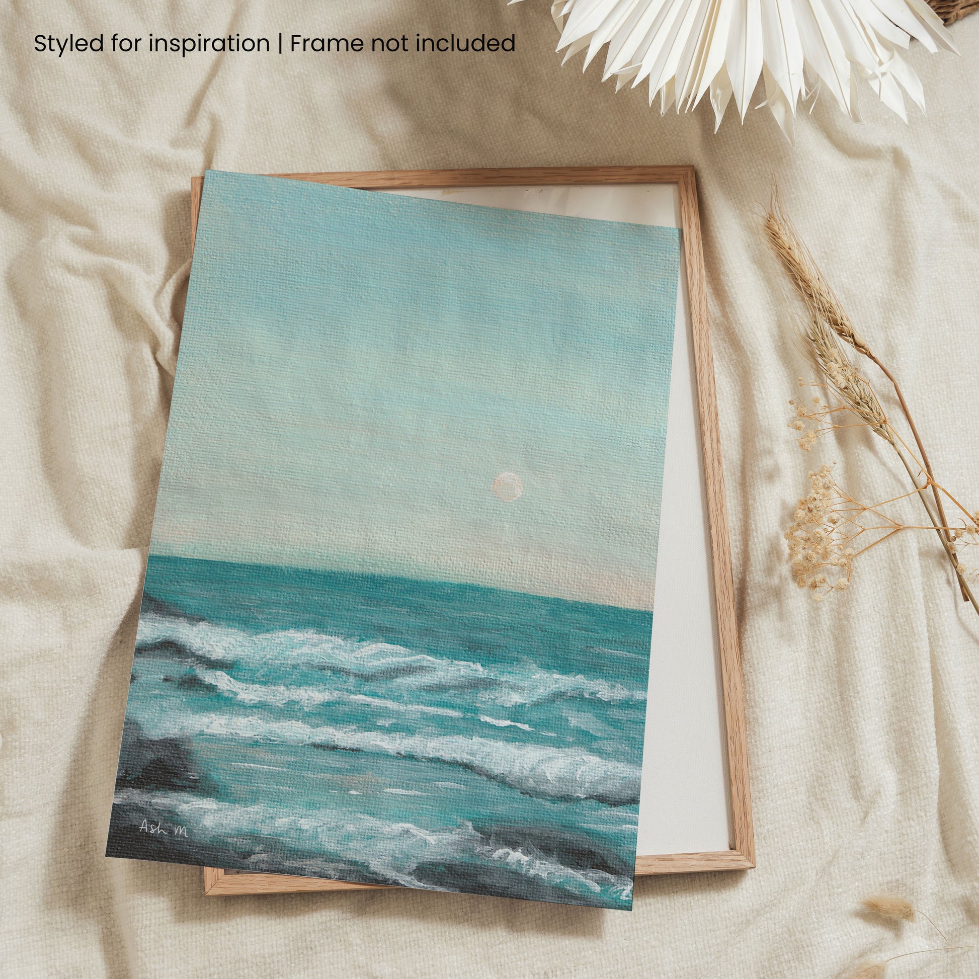 Painting of an ocean and its waves, laid upon a soft tablecloth, with dried flowers on the side.