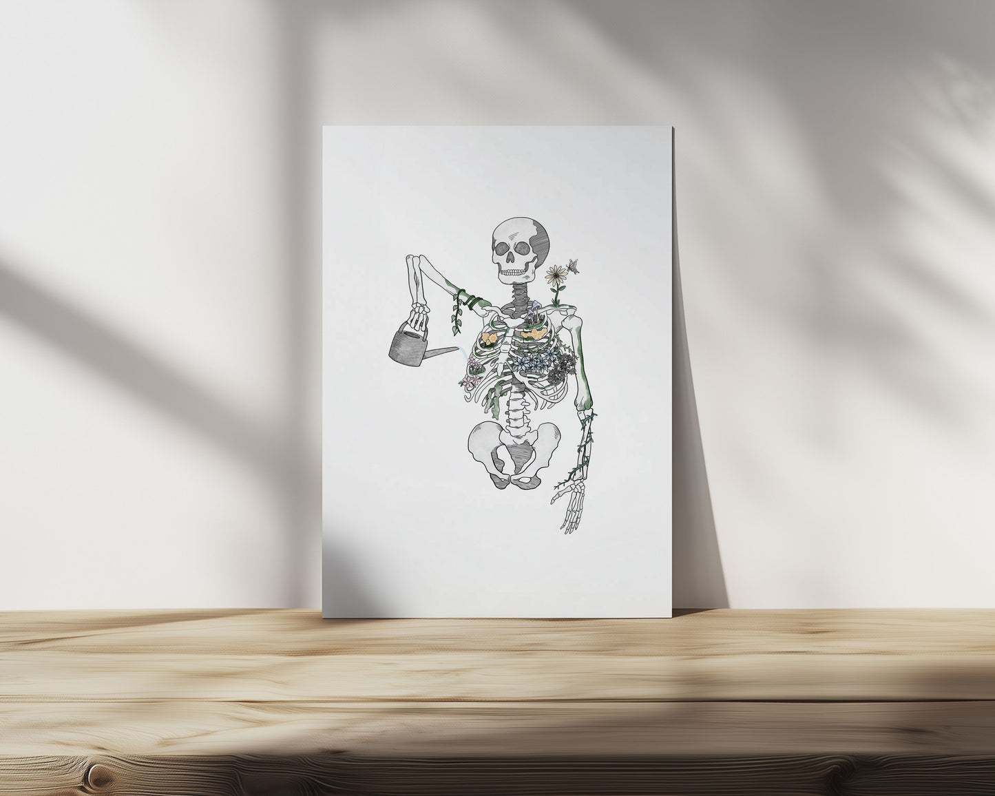 Skeleton with flowers growing from it, holding a watering can to itself  on a white sheet of paper on a wooden surface with a light background.